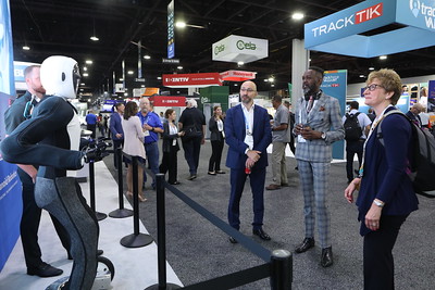 Two men and one woman look at humanoid robot at convention.